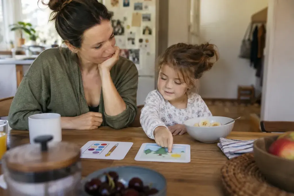 Parent and child choosing between two simple activity cards at a breakfast table, warm ordinary household.